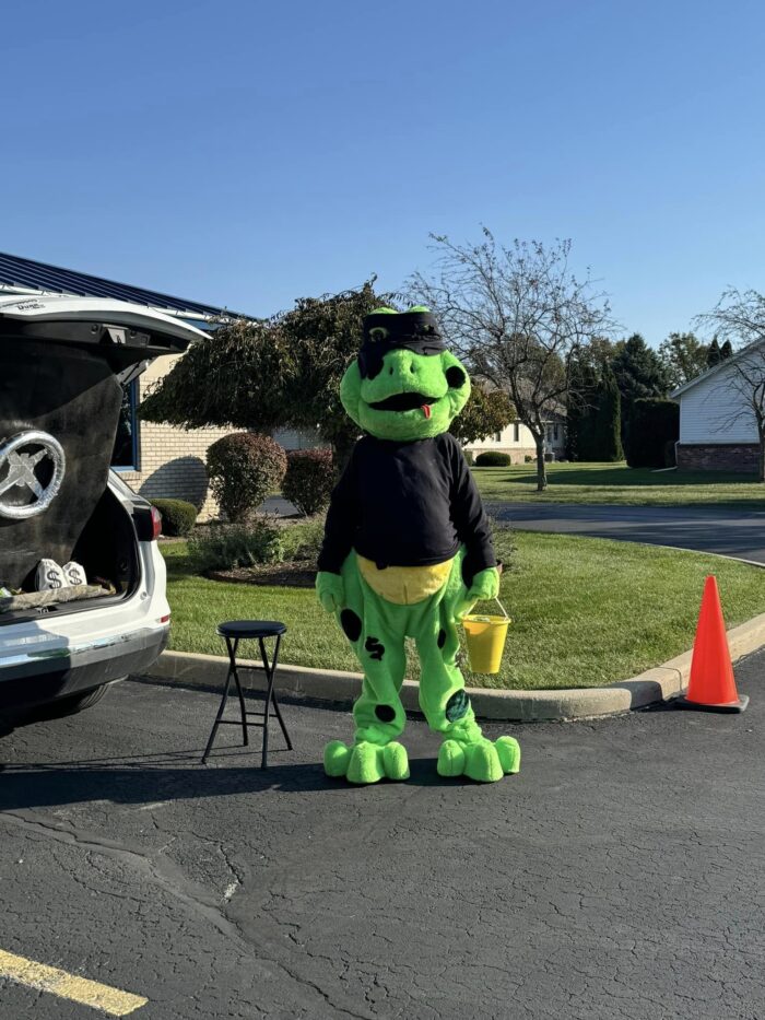 giant frog mascot dressed as a robber holding a bucket of candy