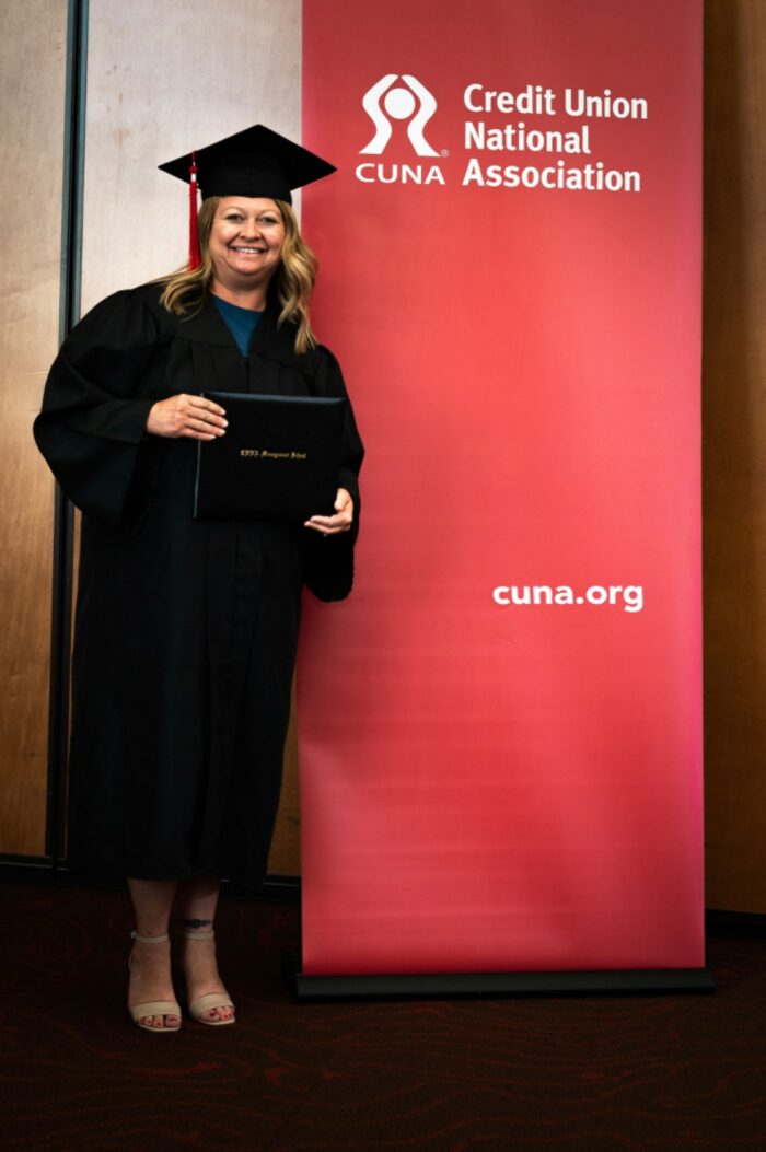 Farrah McGowan in commencement gown and cap in front of CUNA banner
