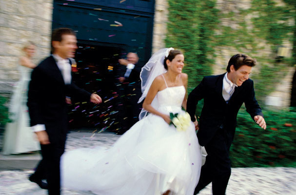 Newlywed couple exiting church surrounded by guests throwing confetti