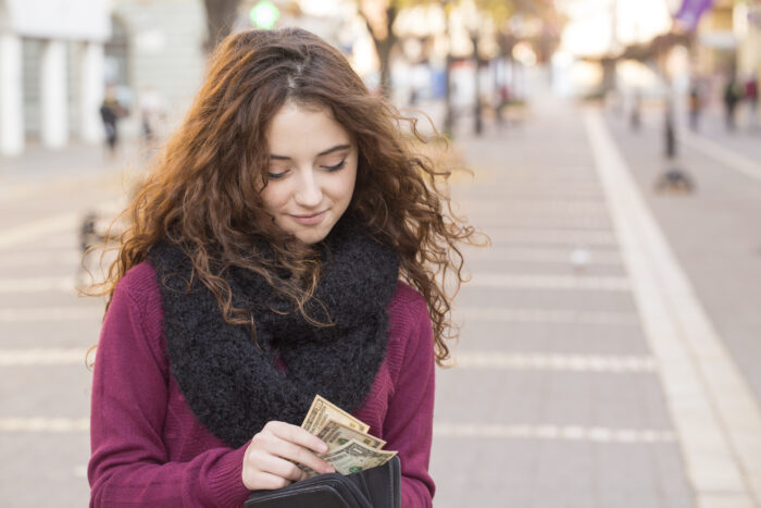 Woman walking on a city street putting cash in her wallet