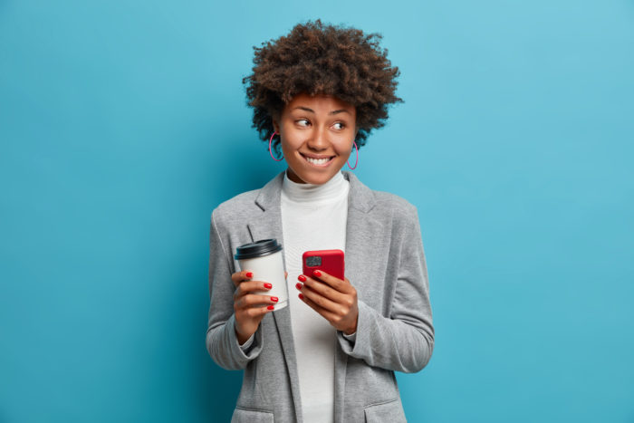 Young lady biting her bottom lip while holding coffee and phone.